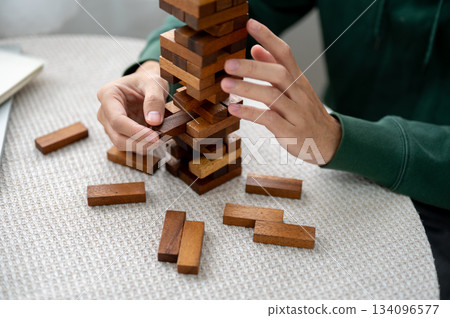 Close up of man's hand pulling out a pieces of wooden block in tower building game as playing alone. 134096577