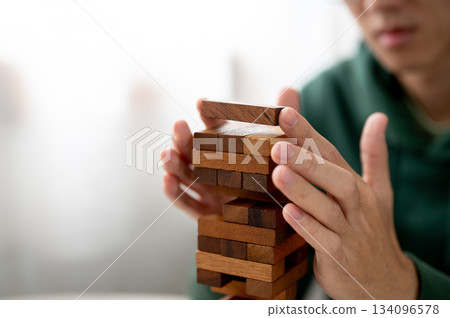 Close up of man's hand putting a wooden block on top in tower building game while playing alone. 134096578