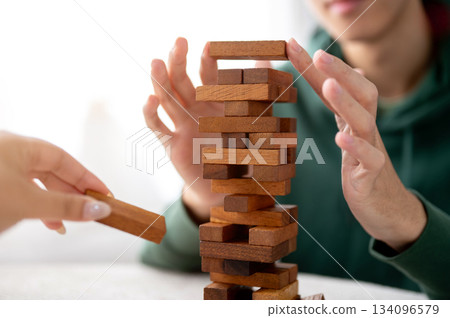 Close up man's hands putting a wooden block on top in tower building game while playing with friend 134096579