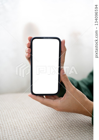 Close up a man holding and showing a blank screen phone with both hands at table in cafe or library. 134096594