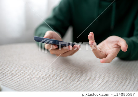 Close up of a man's hand holding phone with an open palm curious gesture on table in cafe or at home 134096597