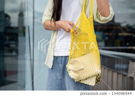 Close up asian woman putting smartphone in a yellow net bag while standing in front of shopping mall Close up asian woman putting smartphone in a yellow net bag while standing in front of shopping mall 134096944
