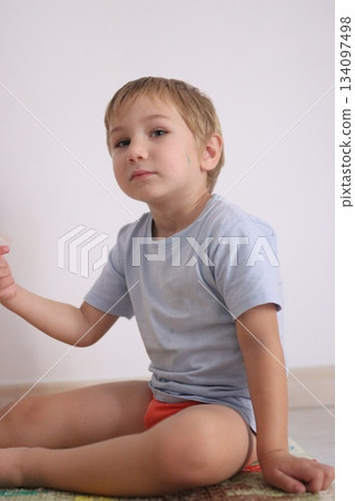 Curious young boy sitting on the floor inside room 134097498