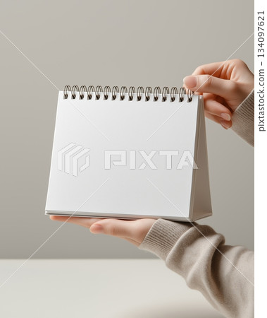 Clean tabletop calendar mockup with spiral ring. Blank paper, hand hold, soft neutral background. Perfect for brand presentation, schedule design, office stationery, planner cover. 134097621