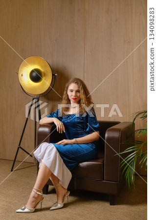 Woman sitting on sofa in blue dress with lights in indoor setting at evening 134098283