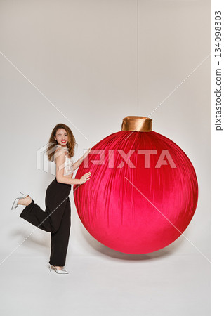 Woman posing with a large red ornament in a studio setting during a holiday theme 134098303