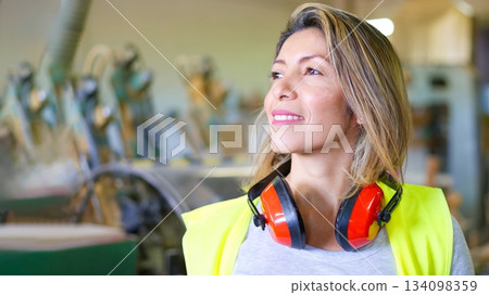 Woman industrial worker wearing safety vest and earmuffs 134098359