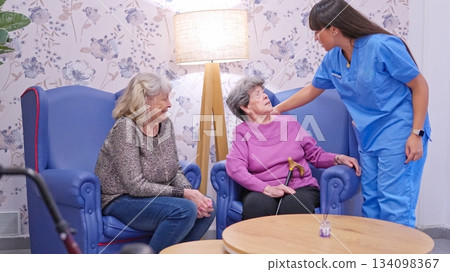 Nurse caring for elderly women in nursing home lounge 134098367