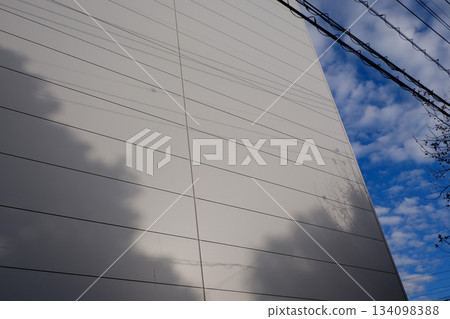 Blue sky, white clouds, and the shadows of trees reflected on the exterior walls of buildings 134098388