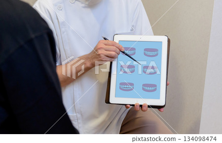A dentist explains the bite and treatment plan using a dental chart on a tablet A dentist explains the bite and treatment plan using a dental chart on a tablet 134098474