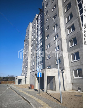 Tall modern concrete residential building against blue sky. Contemporary multi-storey gray concrete apartment block with many windows. Urban residential architecture in a new district 134098748