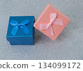 Two small boxes with ribbons are placed on a shiny surface. One box is blue and the other is pink. These boxes are ready for gifting during a party or event. 134099172