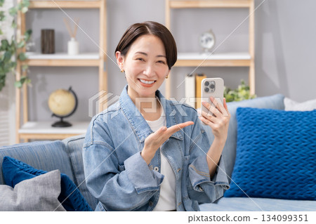 Woman holding a smartphone, waving her hand 134099351