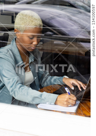 African American woman with short blond hair sits at table and types on laptop. 134100597