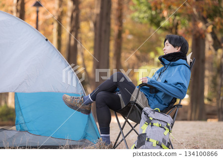 一位獨自露營的男士在秋日營地的椅子上放鬆身心，享受戶外時光，欣賞美景。 134100866