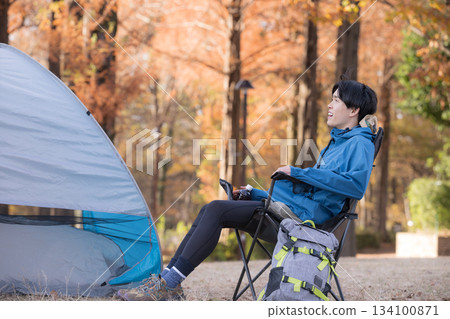 一位獨自露營的男士在秋季露營地的椅子上放鬆身心,享受戶外樂趣。 一位獨自露營的男士在秋季露營地的椅子上放鬆身心,享受戶外樂趣。 134100871