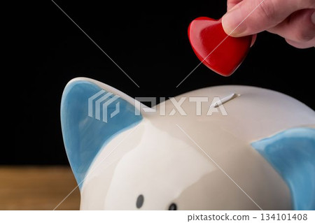 Hand putting red heart coin in piggy bank Hand putting red heart coin in piggy bank 134101408