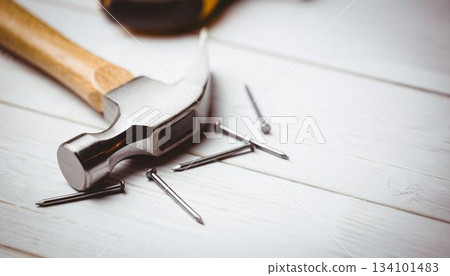 Flat design claw hammer and scattered nails are resting on painted white wooden plank surface Flat design claw hammer and scattered nails are resting on painted white wooden plank surface 134101483