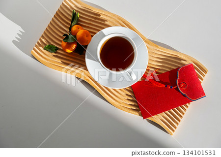 Herbal tea in white cup with tangerine and red envelope on wooden tray. Herbal tea in white cup with tangerine and red envelope on wooden tray. 134101531