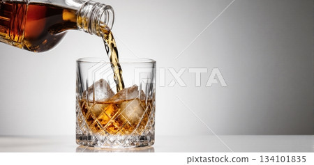 Smooth whiskey pour into an ice-filled glass with a clean white background 134101835