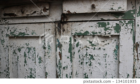 A fragment of an old chest of drawers or sideboard with the texture of the doors and drawers highlighted with peeling, flaking, peeling white paint, abandoned antique furniture A fragment of an old chest of drawers or sideboard with the texture of the doors and drawers highlighted with peeling, flaking, peeling white paint, abandoned antique furniture 134101935