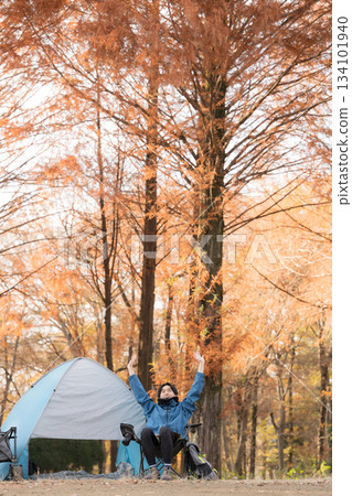 Male solo camper relaxing in a chair at autumn camp, outdoor fun - stretching Male solo camper relaxing in a chair at autumn camp, outdoor fun - stretching 134101940