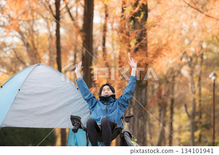 Male solo camper relaxing in a chair at autumn camp, outdoor fun - stretching 134101941