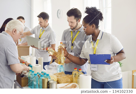 Diverse volunteers group sorting donations of foodstuffs in cardboard boxes for charity food drive 134102330