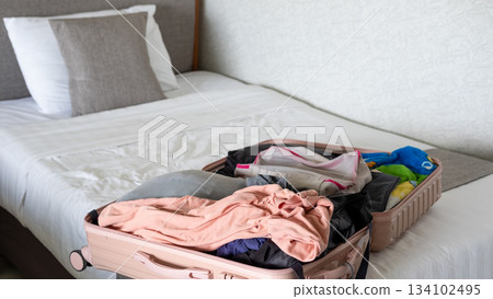 Traveler packing an open suitcase on the bed, organizing essentials for an upcoming journey 134102495