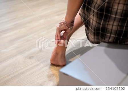Relaxed Asian woman massaging her sore ankle near her bed, highlighting comfort and pain relief Relaxed Asian woman massaging her sore ankle near her bed, highlighting comfort and pain relief 134102502