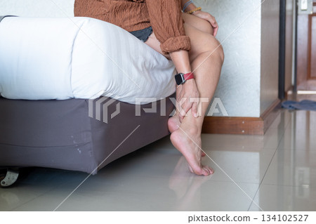 Young Asian woman massaging her ankle on the bed, soothing pain relief and peaceful relaxation 134102527