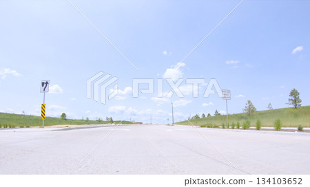 The end of a paved road in Castle Rock, Colorado features caution signs and is flanked by trees. The road leads to a residential area visible in the distance. 134103652