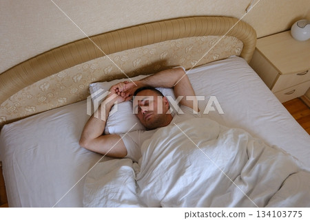 Caucasian man guy lying on bed wake up stretching rubbing eyes male home bedroom good morning sleepy awake wellbeing comfortable new day householder relaxed awakening weekend apartment hotel resting 134103775