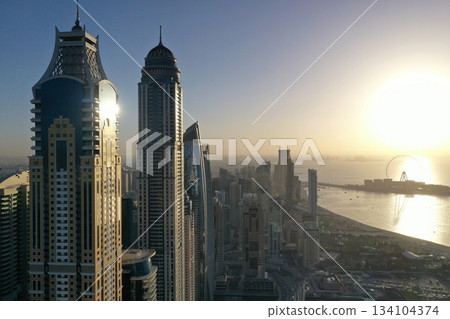 Panoramic aerial view of Dubai Marina skyscrapers and Jumeirah Beach Residence at sunset, featuring the Ain Dubai Ferris wheel and the Arabian Gulf coastline. Panoramic aerial view of Dubai Marina skyscrapers and Jumeirah Beach Residence at sunset, featuring the Ain Dubai Ferris wheel and the Arabian Gulf coastline. 134104374