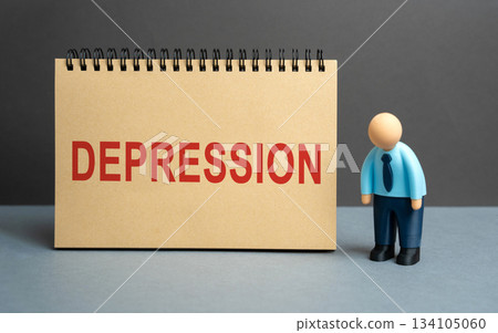 Tired businessman stands near a notebook with the word Depression. Symbolizing mental health issues, stress, burnout, and emotional exhaustion at work. Tired businessman stands near a notebook with the word Depression. Symbolizing mental health issues, stress, burnout, and emotional exhaustion at work. 134105060