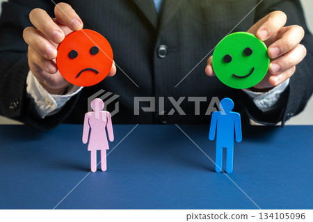 Psychologist holds a happy and angry emoji over a man and a woman. Symbol of conflicts, doubts, and therapy solutions. Suitable for family counseling, psychology, and personal relationship improvement 134105096