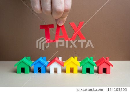 Real estate and housing taxes concept. Business and finance. Taxation. Money, savings. Colorful houses and the inscription Tax in male hand. 134105203