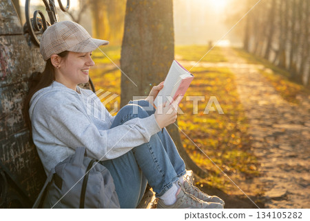 A happy 31 year old caucasian brunette woman reads a book while sitting on a park bench A happy 31 year old caucasian brunette woman reads a book while sitting on a park bench 134105282
