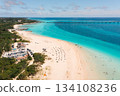 Tourists enjoy a sunny day at a tropical beach with clear blue waters and a long bridge 134108236