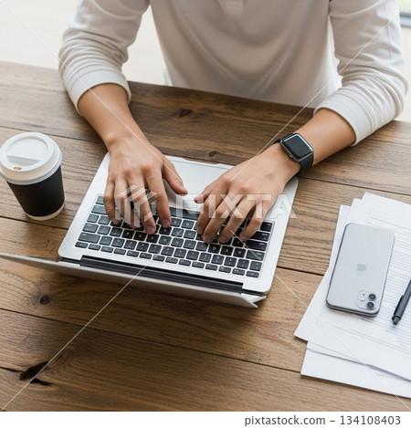 Man's hands working or doing tasks using a laptop at a wooden desk (business, remote work, working from home) 134108403