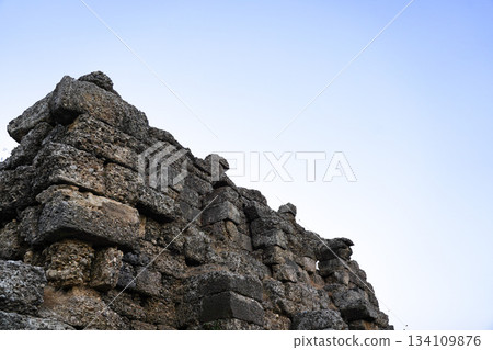 Ancient Stone Wall Remains Under Clear Blue Sky Showcasing Historical Architecture and Weathered Craftsmanship of a Bygone Era Ancient Stone Wall Remains Under Clear Blue Sky Showcasing Historical Architecture and Weathered Craftsmanship of a Bygone Era 134109876