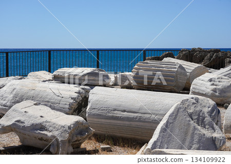Ancient Ruins by the Sea: Weathered Columns and Fragments Along the Coastline against a Clear Blue Sky 134109922