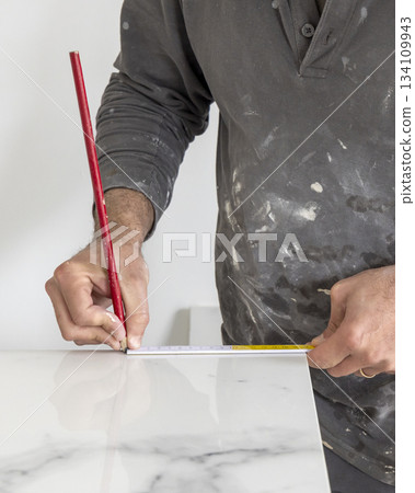 Craftman in grey shirt measures a marble tile using a ruler. Handy men at work, hands closeup Craftman in grey shirt measures a marble tile using a ruler. Handy men at work, hands closeup 134109943