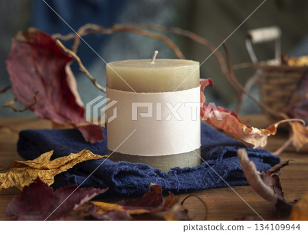 Candle with a label near autumn dried leaves closeup, fall mockup in blue, red and orange Candle with a label near autumn dried leaves closeup, fall mockup in blue, red and orange 134109944
