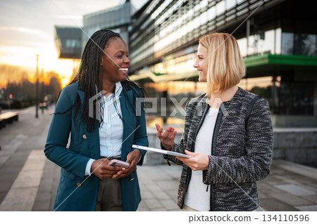 Diverse businesswomen discussing work outdoors during sunset Diverse businesswomen discussing work outdoors during sunset 134110596