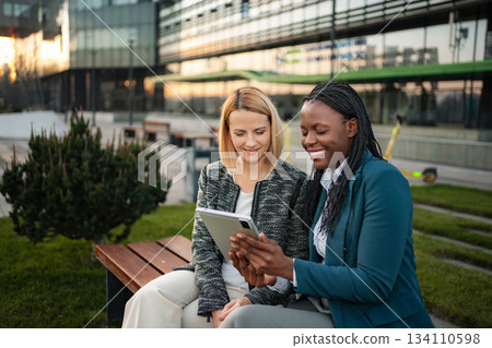Diverse businesswomen collaborating outdoors with digital tablet 134110598