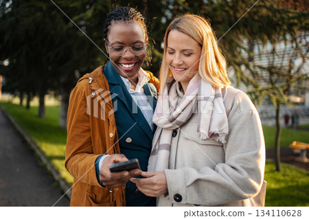 Diverse women friends smiling sharing content on smartphone 134110628