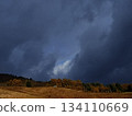 Late autumn mountain forests and fields illuminated by the setting sun with heavy, dark rain clouds on their backs 134110669