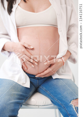 Expecting mother gently cradles her baby bump indoors Expecting mother gently cradles her baby bump indoors 134110751