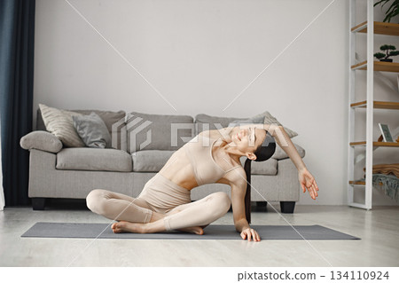 Attractive young woman doing yoga stretching at home. Brunette woman wearing beige leggins and top. Self-isolation is beneficial, entertainment and education on the Internet. Attractive young woman doing yoga stretching at home. Brunette woman wearing beige leggins and top. Self-isolation is beneficial, entertainment and education on the Internet. 134110924
